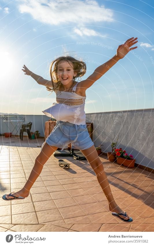 Pretty little girl dressed in a white tank top dancing and jumping on the house terrace at sunset nature happiness sky beautiful playing hand light cute tot