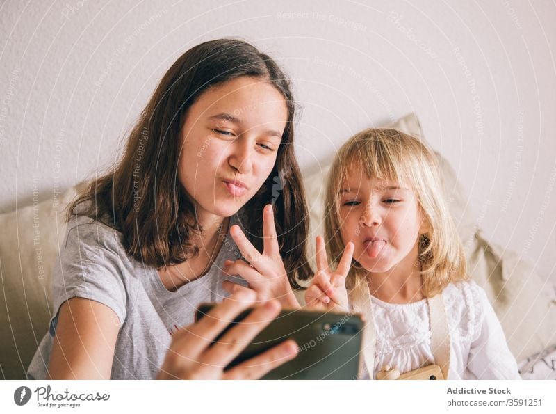 Cheerful sisters taking selfie on smartphone at home grimace girl sibling using v sign having fun gesture teenage little peace two fingers charming content