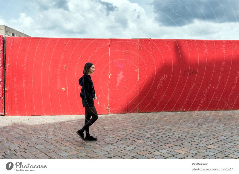 Young woman runs in front of red wall with shadow girl Red Wall (building) Construction site Shadow Sky Sun Clouds Town pavement urban smile Woman Potsdam