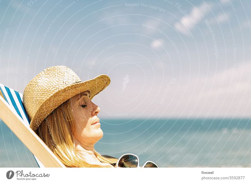 woman resting on a lounger in the sun, french coast surfer borsalino hat enjoying summer sun people blonde sea lifestyle portrait face poses attractive shore