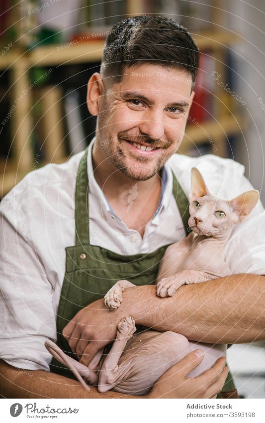 Happy adult man with Sphynx cat in workshop artisan smile workroom happy pet uniform studio hairless companion workman owner male joy sphynx animal designer