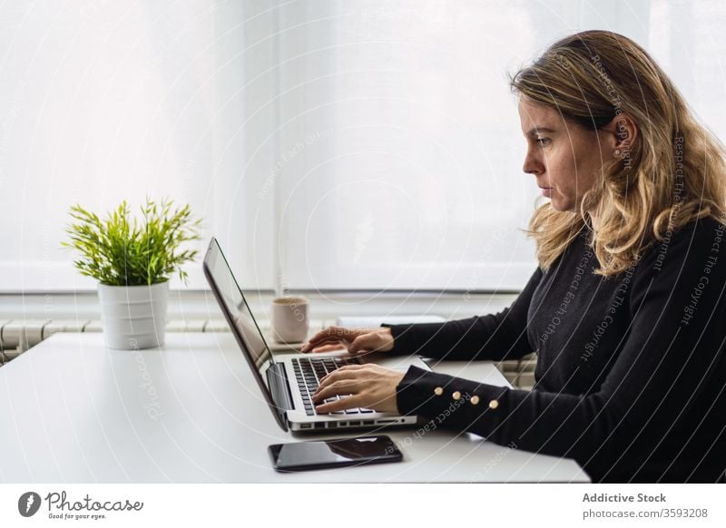 Young woman working with laptop at home online remote table casual busy young female workplace freelance device gadget internet write notebook modern job focus