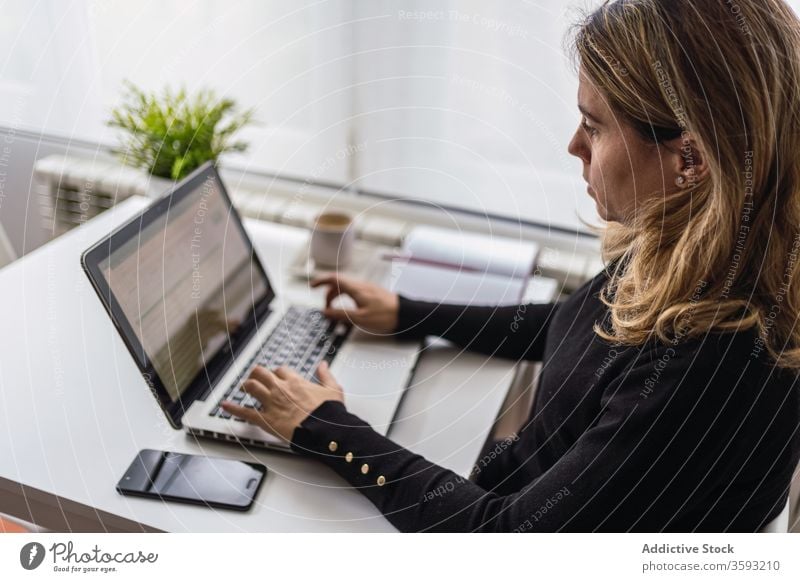 Young woman working with laptop at home online remote table casual busy young female workplace freelance device gadget internet write notebook modern job focus