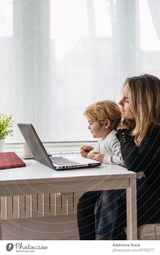 Woman with little kid working on laptop at home woman mother using together online busy remote child curious point motherhood interact parent female