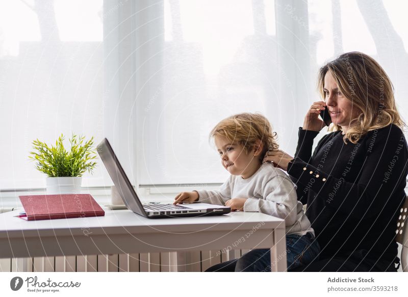 Woman with little kid working on laptop at home woman mother using together online busy remote child curious point motherhood interact parent female