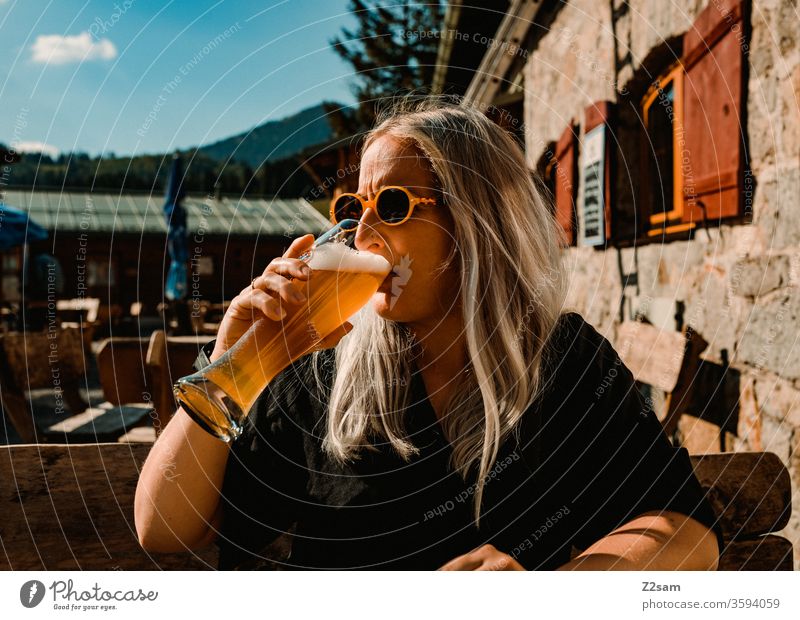 Young woman drinking a wheat beer at the mountain hut alpine hut mountains Alps Drinking enjoyment white beer Beer teen Blonde long hairs sunglasses Lifestyle