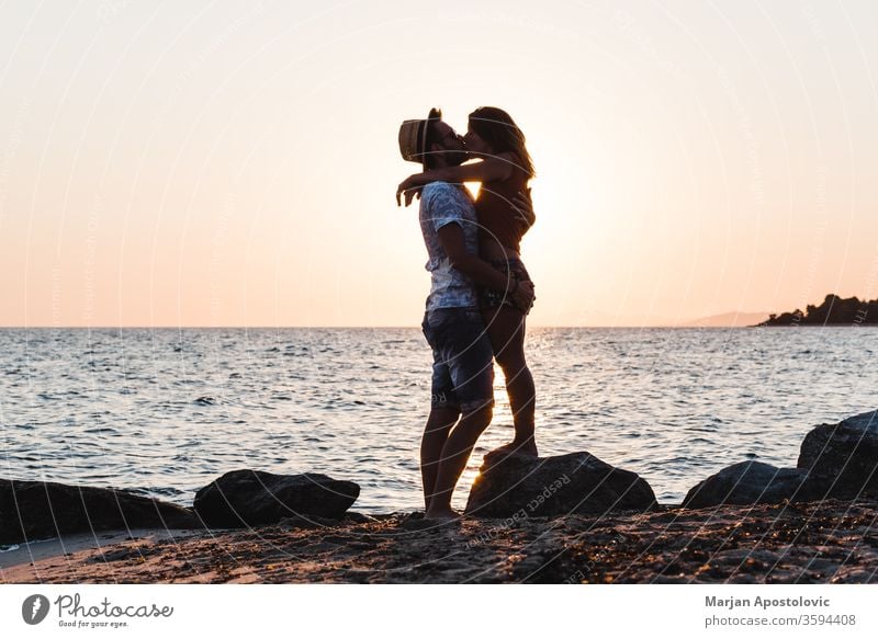 Young couple kissing on the beach in sunset young man woman love sea ocean honeymoon lovers newlyweds romance romantic casual travel holiday summer coastline