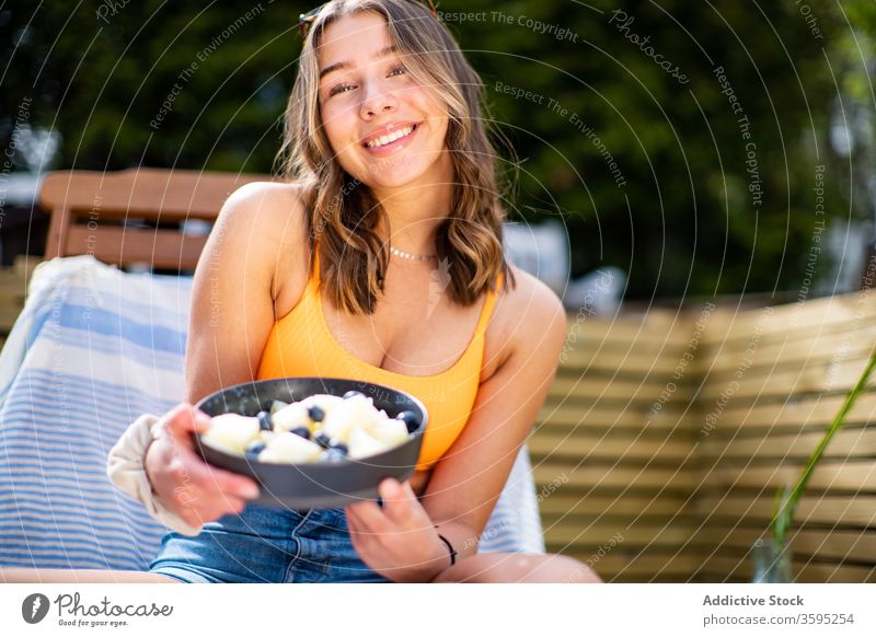 Smiling woman with bowl of fresh fruits summer chill berry smile deckchair terrace female cheerful relax rest sit ripe wooden veranda comfort glad holiday lady