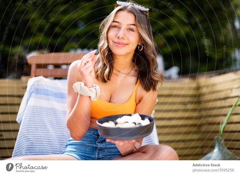 Smiling woman with bowl of fresh fruits summer chill berry smile deckchair terrace female cheerful relax rest sit ripe wooden veranda comfort glad holiday lady