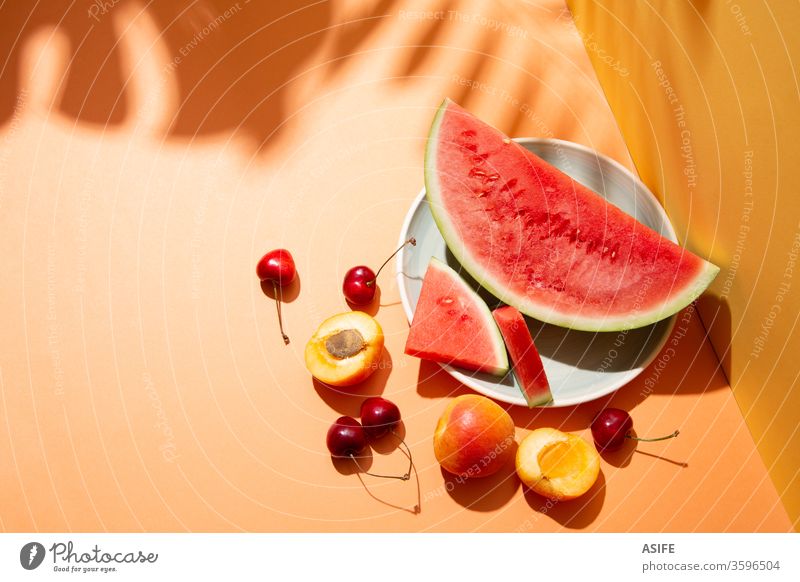 Summer fruit composition with tropical leaves shadows on orange background summer colorful watermelon still life palm cherry apricot yellow copy space monstera