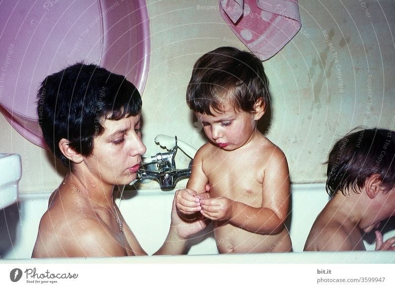 old l Young, pretty, attractive mother with short, black hair, bathes together with her two children in the bathtub of the 60s Caring, attentive mom, cares lovingly, interested, turned to question from curious child.