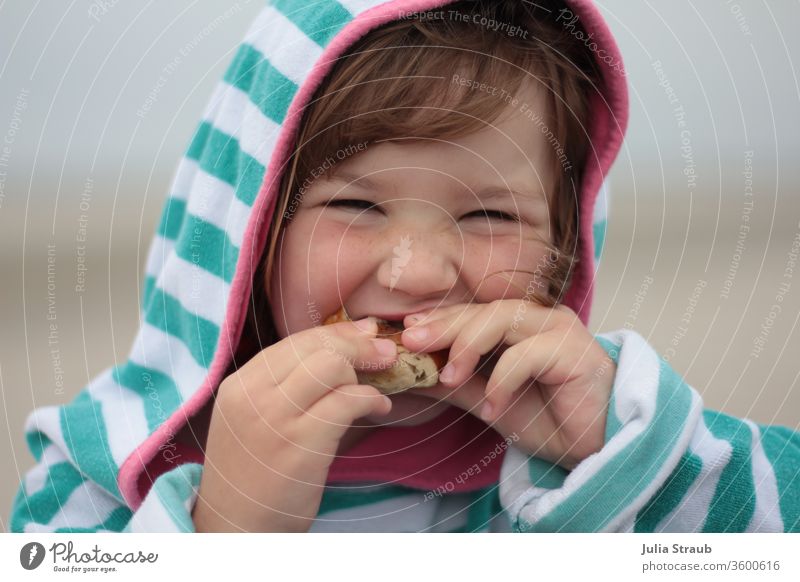 Girl with hooded towel eating a bun girl Toddler Freckles Towel Hooded (clothing) grinning Eating Bite stop Roll roll Laugenbrötchen Striped Striped sweater