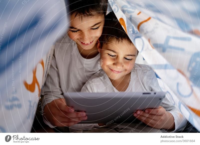 Happy brothers watching video on tablet together cartoon sibling pajama blanket using hide enjoy home daytime interesting positive kid bed boy childhood