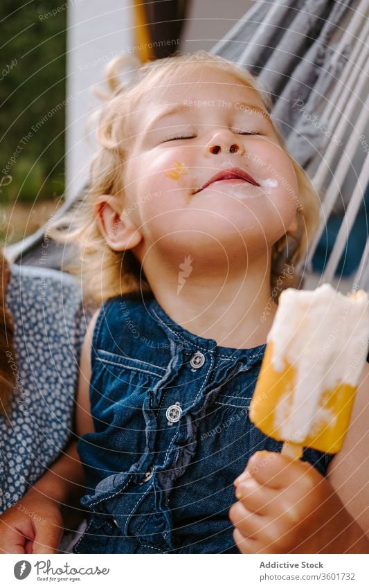 Dreamy girl with ice cream in hammock eat popsicle summer terrace homemade kid little content child childhood relax carefree enjoy adorable cheerful chill food