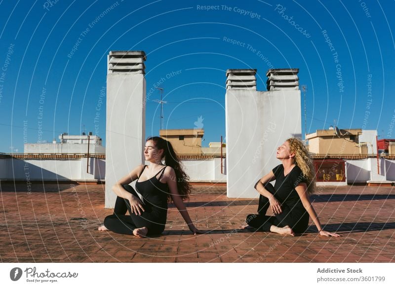 Women practicing yoga together on rooftop women terrace practice pose position ardha matsyendrasana twist half lord of the fishes acro yoga mother daughter