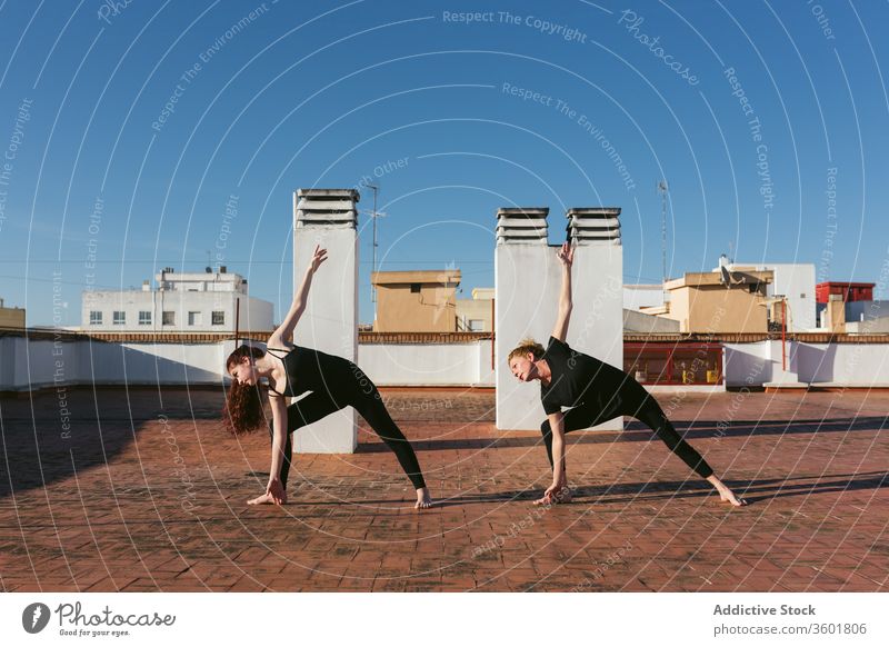 Women practicing twist yoga pose on rooftop women together practice revolved triangle parivrtta trikonasana stand position stretch balance terrace lifestyle