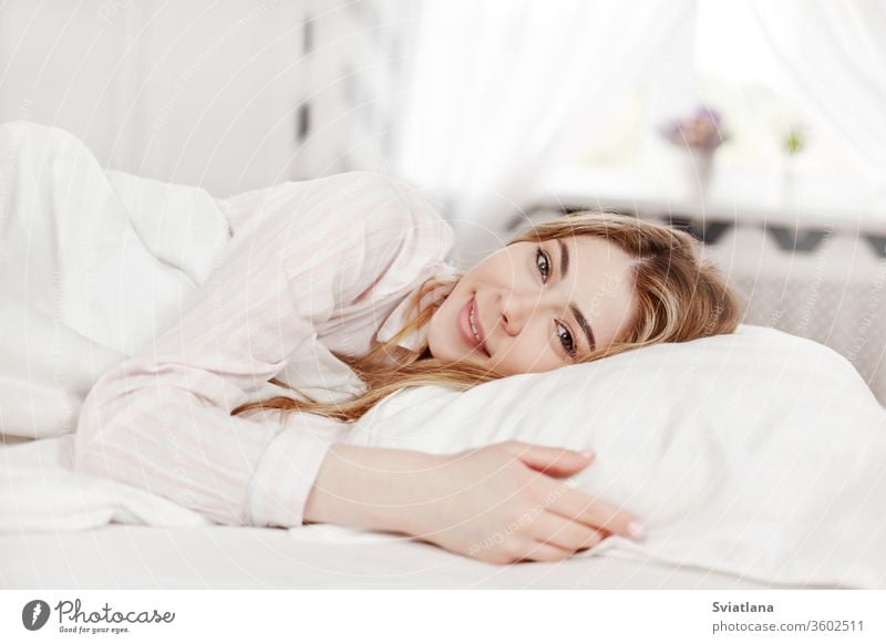 A young attractive girl in striped pajamas is lying in bed in her bedroom in the morning . Side view woman beautiful home sleeping female pillow relaxation calm