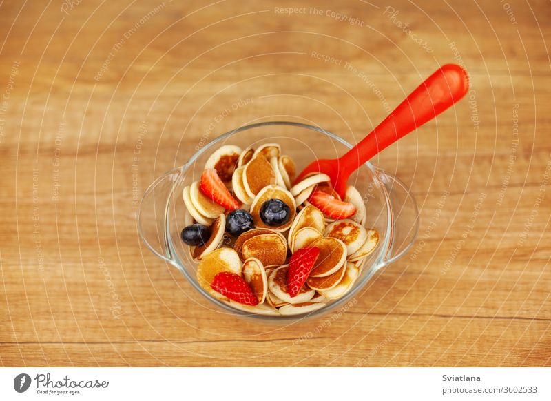 Mini pancakes with strawberries and blueberries in a bowl on a wooden table, top view. Trendy food - pancake cereal mini background trendy fresh tasty cooking