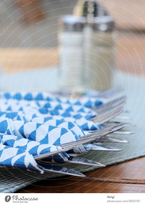 Enjoy your meal. - Cutlery - knife and fork - wrapped in blue and white napkins is lying on a table, salt and pepper shakers in the background Knives Fork