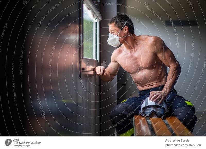 Muscular fireman in protective respirator at fire station firefighter safety work mature helmet male strong naked torso serious sit bench wooden muscular