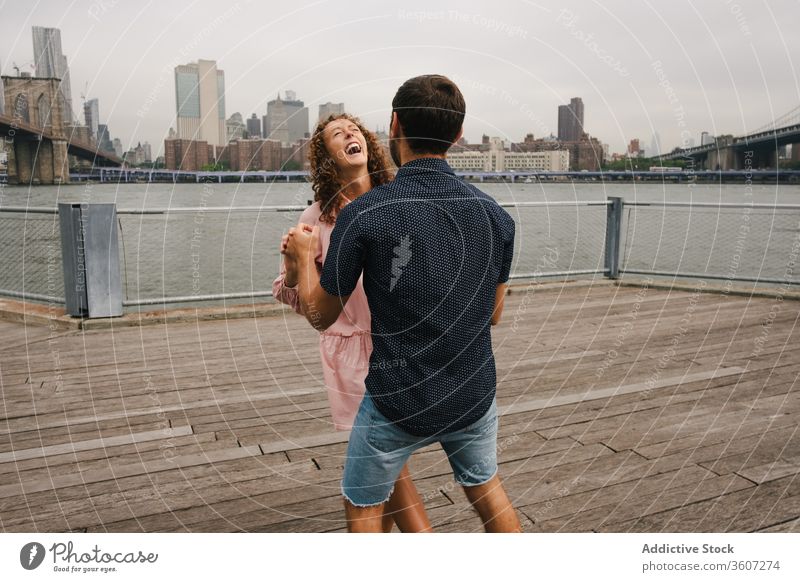 Happy couple dancing on embankment embrace promenade stroll city cheerful dance relationship river hug brooklyn bridge motion new york america united states usa
