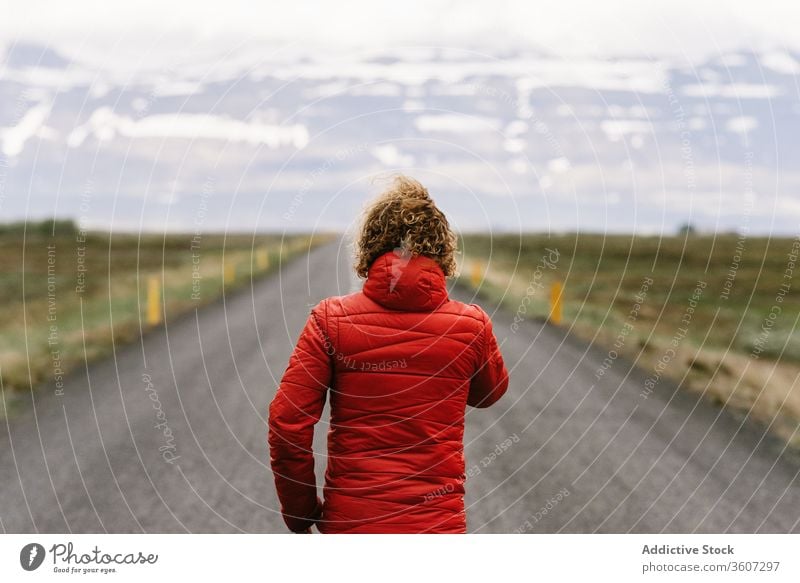 Lonely anonymous male tourist walking along road traveler mountain man roadway scenic asphalt winter iceland empty scenery nature adventure snow cold season