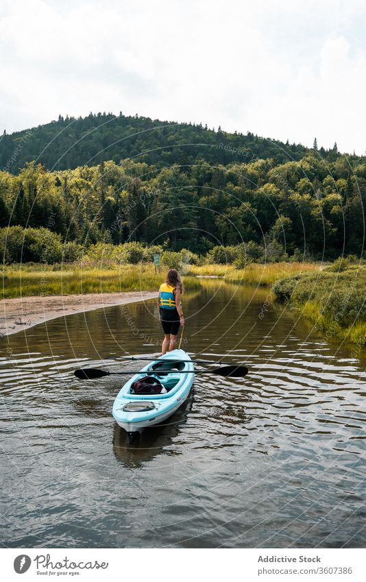Anonymous woman with boat standing in river hill nature admire travel national park la mauricie quebec canada clean coast kayak water green trip journey