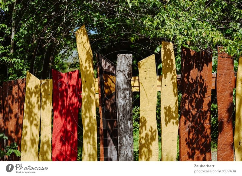 Colourful wooden fence with yellow, brown and red slats, leaves and shadow Fence Wooden fence variegated Yellow Brown Red wooden slats tree Shadow Contrast