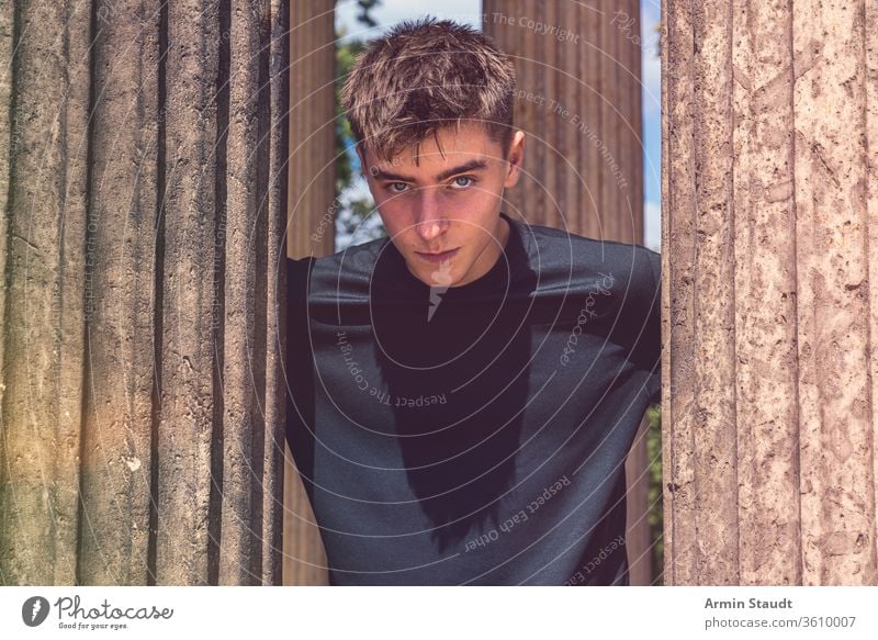 portrait of a young man standing between ancient columns teenager lifestyle architecture beautiful black blue boy casual caucasian clothes concentration