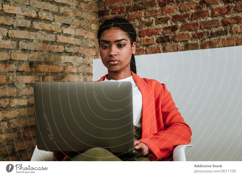 Modern black woman with computer in armchair business laptop online elegant loft design focus interior freelance modern device gadget internet using browsing