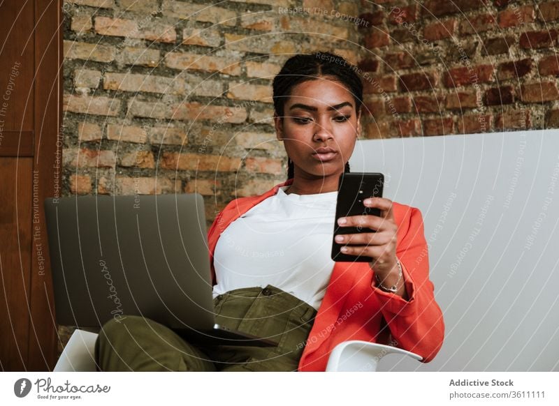 Modern black woman with gadgets in armchair business laptop cheerful smartphone online elegant computer loft design interior freelance modern happy device