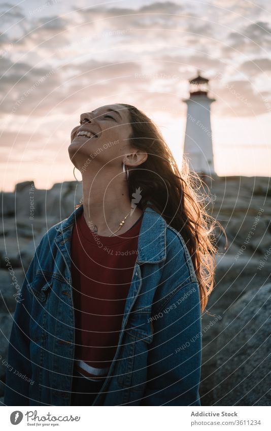 Happy woman against sunset sky and lighthouse happy travel laugh cloudy peggys cove canada female young sundown evening dusk twilight smile casual joy cheerful