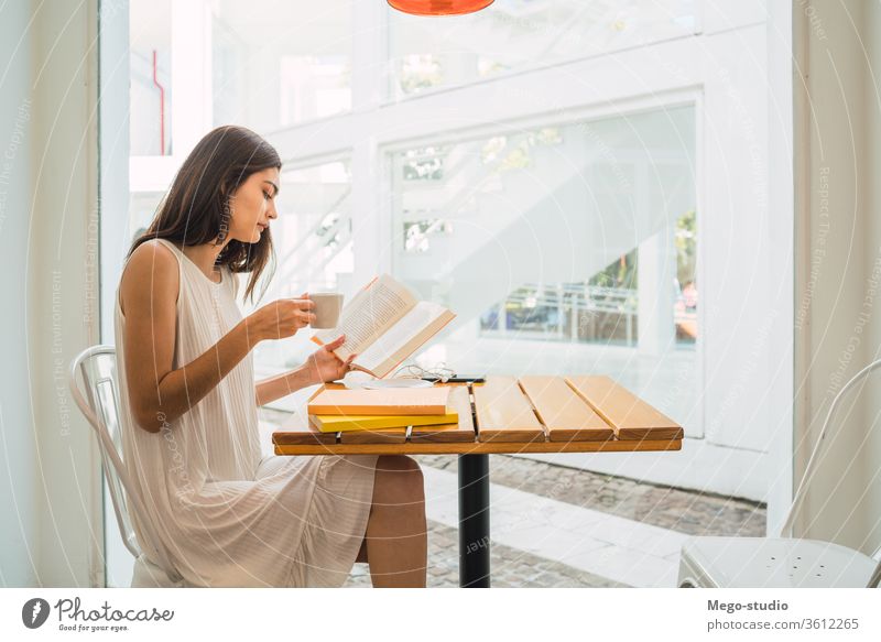 Young woman reading a book at coffee shop. female sitting relaxing hobby serious culture coffee break caucasian looking pensive textbook portrait learn
