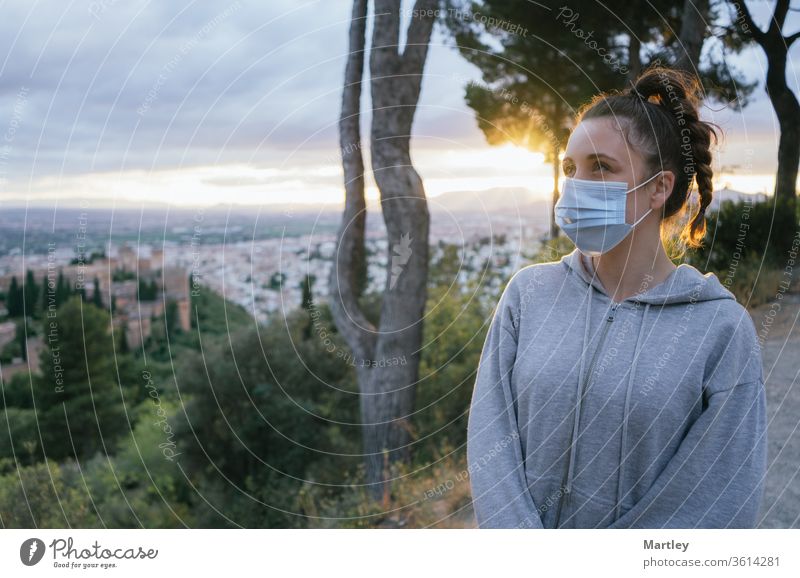 Young girl looking with a mask by the covid, pollution with the sun in the background, above the city of the Alhambra, Spain. Summer sunset with sunlight.