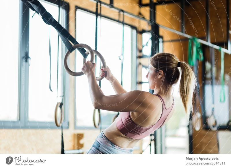 Young sporty woman training on gymnastic rings muscular arms holding indoor fit fitness tough endurance one people focused power young blonde workout strength