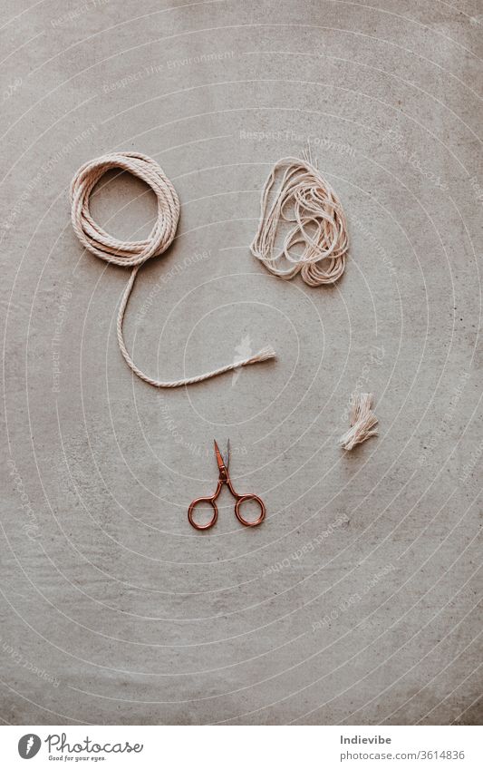 A small rose gold scissor and a piece of rope on grey background hobby diy cut scissors activity break closeup concept craft creative design divide eco friendly