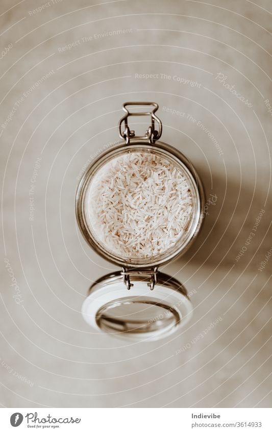 Top view closeup of an open glass jar container full with uncooked rice on grey background food stock bulk air tight basics cooking corona coronavirus dry