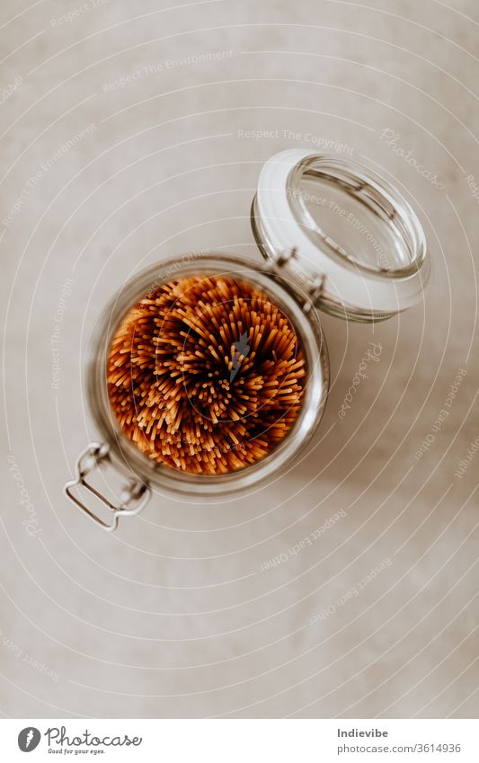 Top view closeup of a glass jar container full with uncooked spaghetti pasta on grey background food pantry air tight basics bulk cooking corona coronavirus dry
