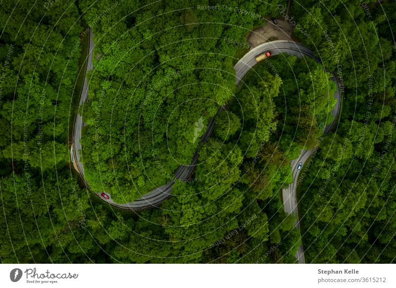 Wonderful green forest with a curvy road and cars from a top view drone shot, aerial of an s curve background which implicates fun of driving or take a trip through the nature.