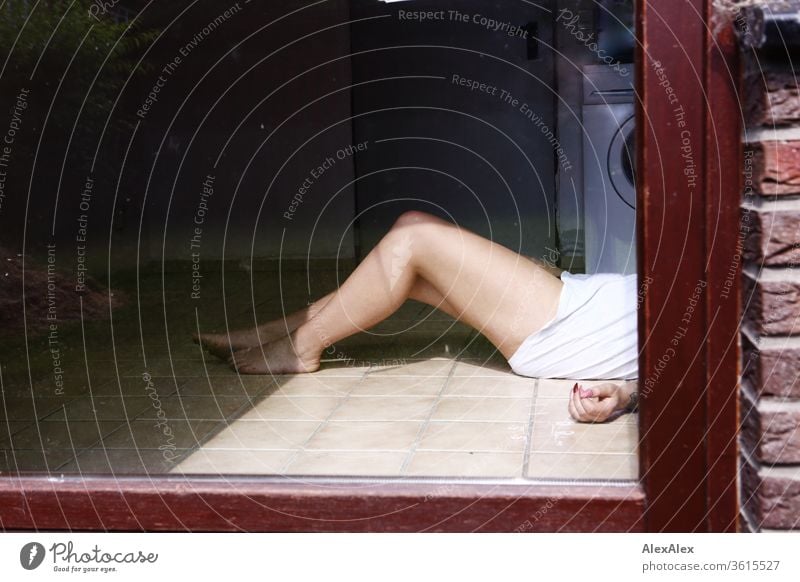 A young woman lies behind a glass door in a washroom, all you can see are her bare legs, one hand and a white T-shirt girl Young woman already Skin youthful 19