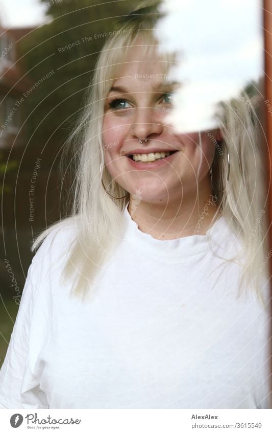 Portrait of a young blonde woman behind a window pane girl Young woman already smile Blonde long hairs blue eyes Skin youthful 19 18-20 years 15-20 years old