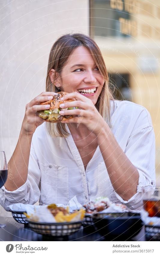 Laughing woman having burger while enjoying lunch with friend cafe cheerful street summer happy communicate interact meal yummy dish cuisine portion sandwich