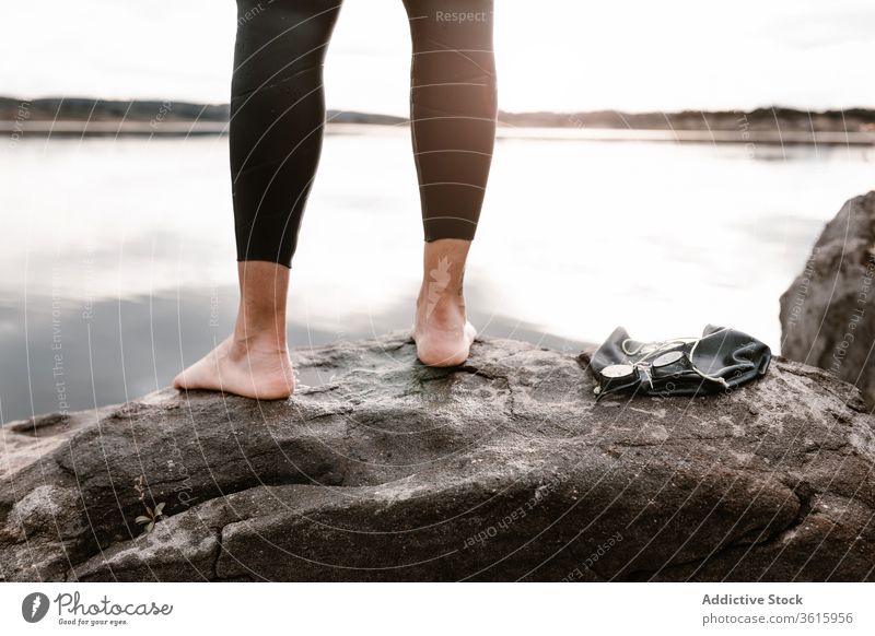 Faceless sportsperson standing barefoot on rock before diving diver wetsuit lake goggles water evening boulder inspiration sunset swimsuit nature shore