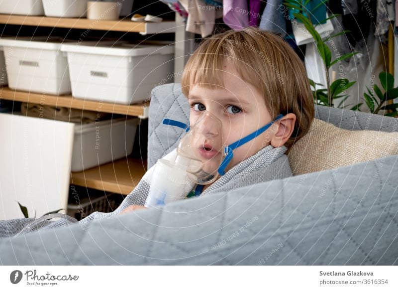 Little caucasian boy making inhalation with nebulizer at home. Child holds a mask vapor inhaler. Treatment of asthma. Concept of inhalation therapy apparatus.