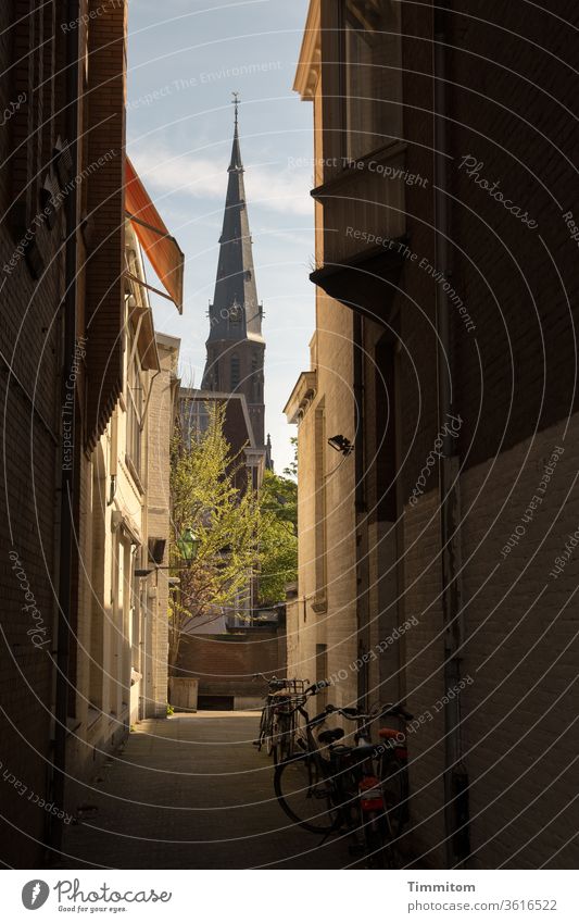 An alley with bicycles and a view of a church tower Alley houses Inputs Window Church spire Sky Blue Shaft of light Netherlands