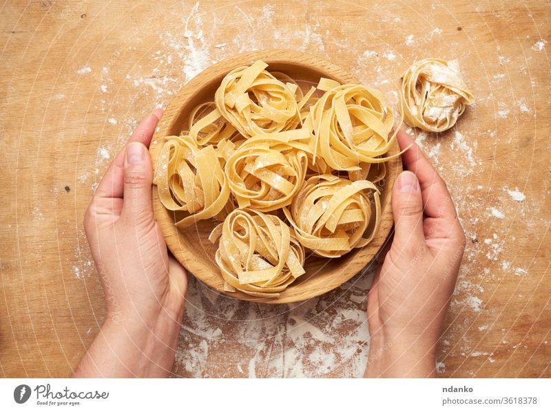 female hands holding a wooden plate with raw fettuccine pasta orange rolled dry flour food fresh heap ingredient italian italy kitchen cooking brown preparing