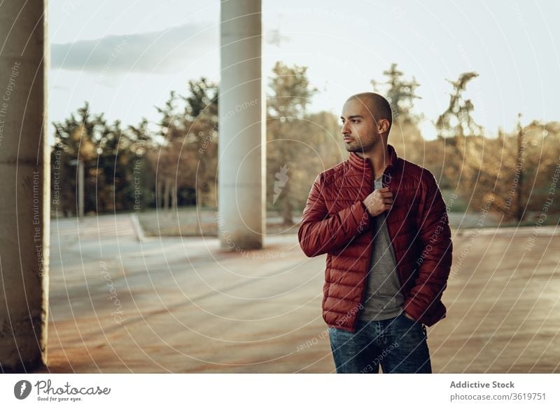 Young man in trendy outfit standing on street young modern confident jacket warm clothes pensive hipster unshaven autumn beard thoughtful think bald male