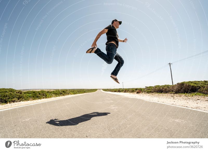 Man happily jumping high above the road man happy algarve portugal cabo de sao vicente cape saint vincent wilderness run perspective possibility effort jeans