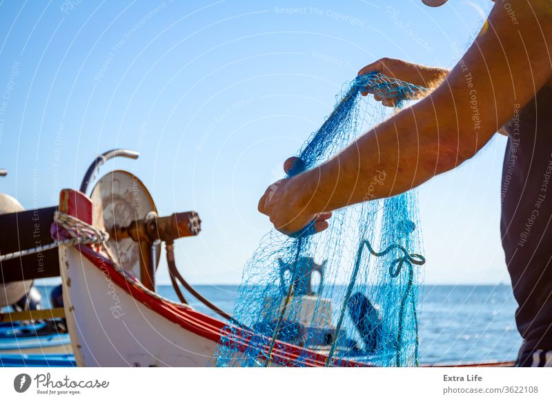 Fisherman is empty fish from net in his small boat - a Royalty