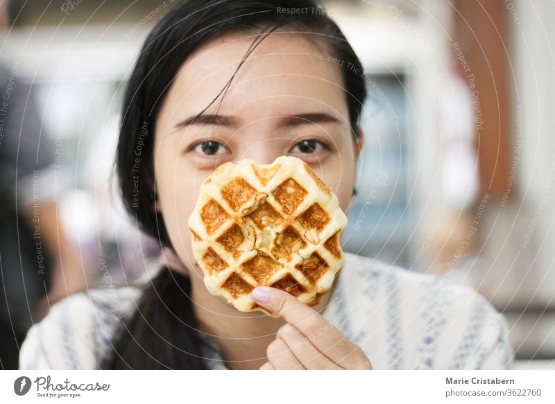 Asian woman holding up a delicious waffle snack happiness smiling lifestyle asian woman real people positivity quirky woman tasty flavor attractive thoughtful